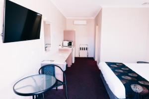 a room with a bed and a table and a tv at Motel Poinsettia in Port Augusta