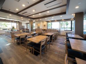 佐久市にあるホテルルートイン佐久南インターの木製のテーブルと椅子、大きな窓のあるレストランを併設しています。