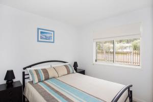 a white bedroom with a bed and a window at Beach Retreat in Mollymook