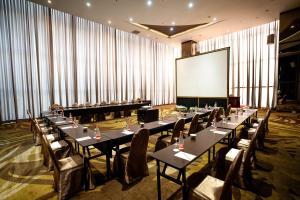 فندق جراندي في باندونغ: قاعة اجتماعات بطاولات وكراسي طويلة وشاشة بيضاء