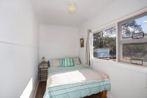 a small bedroom with a bed and a window at Retro Beach Cottage in Kioloa