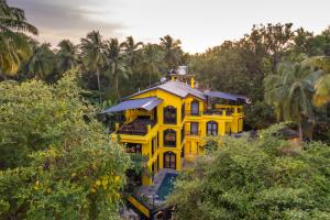 a yellow house in the middle of trees at Whoopers Boutique Hotel, Anjuna in Anjuna