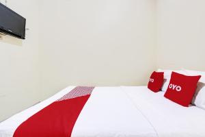 uma cama branca com almofadas vermelhas e uma televisão em OYO 91803 Gita Graha Guest House Syariah em Yogyakarta