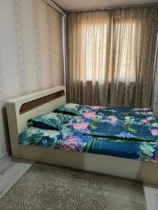 1 Schlafzimmer mit einem Bett mit einer Blumendecke und einem Fenster in der Unterkunft 2 х комнатная квартира in Schymkent