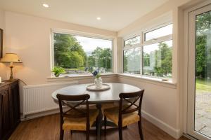 een eetkamer met een tafel en twee stoelen en twee ramen bij Riverside Cottage, Bridge of Balgie, Glenlyon, Perthshire 