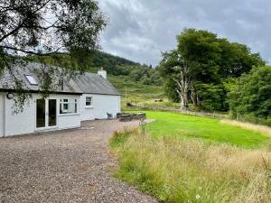 a white cottage with a grassy field next to it at Riverside Cottage, Bridge of Balgie, Glenlyon, Perthshire 