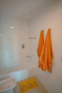 La salle de bains blanche est pourvue de serviettes orange accrochées au mur. dans l'établissement Departamento con vista a las montañas + garage, à Salta