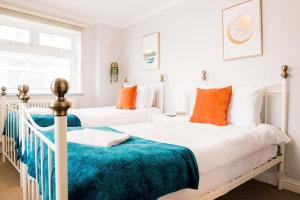 2 bedden in een witte slaapkamer met oranje kussens bij Mumbles Apartment near to shops and beach in The Mumbles