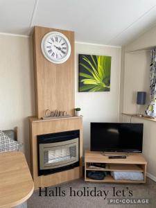 sala de estar con TV y reloj en la pared en Coastfields 3 bed 8 berth holiday home, en Ingoldmells