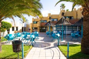une terrasse avec des chaises bleues et des palmiers en face d'un bâtiment dans l'établissement Oeste Tere by Best Holidays Fuerteventura, à Corralejo