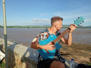 Khajuraho Dreams Homestay في خاجوراهو: رجل يعزف على الغيتار بجوار النهر