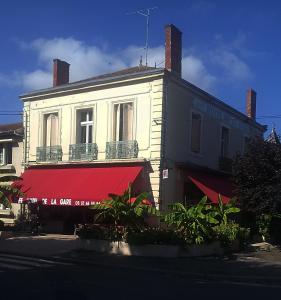 stary biały budynek z czerwoną markizą w obiekcie Hotel Café de la Gare w mieście Sainte-Foy-la-Grande