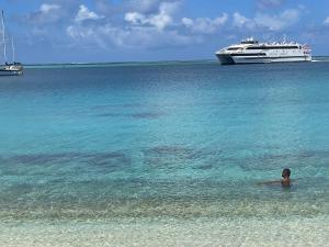 a person swimming in the ocean with a cruise ship at Huahine Beach House in Fare