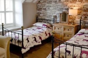 a bedroom with two beds and a stone wall at Woodbank Cottage Newton Stewart in Newton Stewart