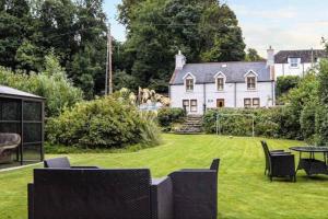 Woodbank Cottage Newton Stewart في نيوتن ستيوارت: منزل به ساحة مع كراسي وطاولة