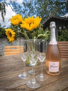 a bottle of champagne and four wine glasses on a wooden table at Duck Cottage - Grade II Listed cottage, village location, nr Holt in Letheringsett