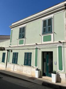 biały budynek z zielonymi okiennicami na ulicy w obiekcie Casa Leone w mieście Buggerru