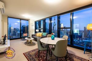 een woonkamer met een tafel en stoelen en grote ramen bij Aussie Escape Apartments in Melbourne