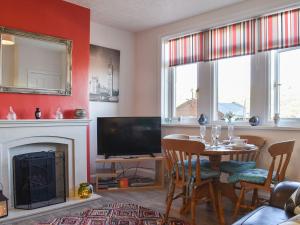 sala de estar con mesa, TV y chimenea en Holme Valley Cottage, en Holmfirth