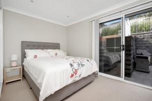 a white bedroom with a bed and a window at Banksia by the Sea Gerroa in Gerroa