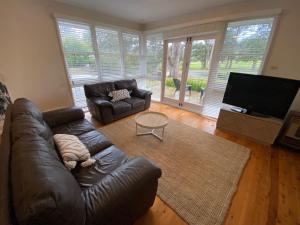 a living room with a leather couch and a flat screen tv at Beach House On Golf in Mollymook