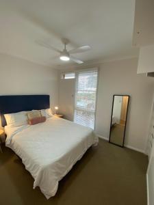 a bedroom with a large white bed with a ceiling fan at Beach House On Golf in Mollymook