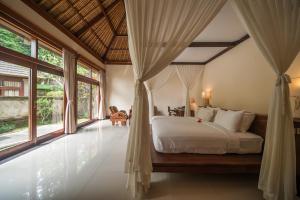 sypialnia z łóżkiem i dużymi oknami w obiekcie The Payogan Villa Resort and Spa w mieście Ubud