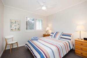 a white bedroom with a bed and a chair at Fathoms 17 in Mollymook