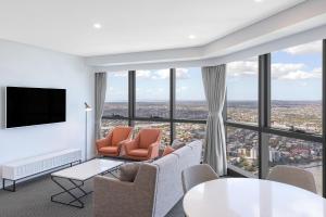 a living room with chairs and a tv and windows at Meriton Suites Adelaide Street, Brisbane in Brisbane