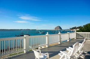 a deck with white chairs and the water and boats at Inn at Morro Bay in Morro Bay