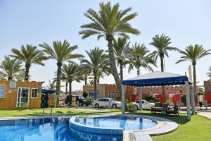 a swimming pool with palm trees and a building at OYO 138 Gulf Sand Motel in Barka