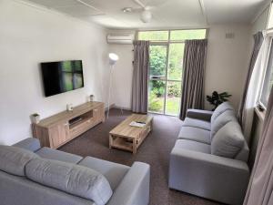 sala de estar con 2 sofás azules y TV en Russell Falls Holiday Cottages, en Parque Nacional