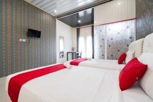 a bedroom with two beds with red pillows and a tv at RedDoorz Syariah near Minangkabau International Aiport in Duku