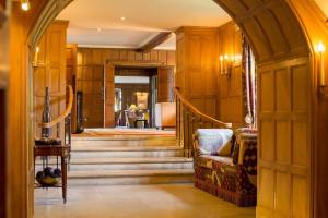 a hallway with wood paneling and stairs with a chair at Whatley Manor in Malmesbury