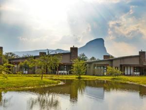 a building next to a river with a mountain in the background at Monomotapa Village @ Legend Golf and Safari Resort in Golders Green