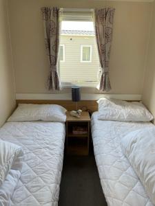 1 dormitorio con 2 camas y una ventana con cortinas en Beautiful Butlins van, en Lincolnshire