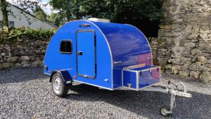 a blue trailer parked next to a stone wall at Darwin Teardrop Caravan for Hire from ElectricExplorers in Hawkshead