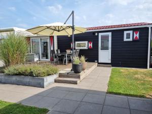 ein schwarzes Haus mit einer Terrasse mit einem Sonnenschirm in der Unterkunft Chalet Serooskerke SE09 in Serooskerke