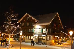 un grand bâtiment avec des personnes debout à l'extérieur le soir dans l'établissement Posthotel Rössli, à Gstaad