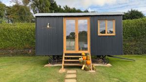 a black tiny house sitting on top of a field at Shepherds Hut at Cedar Gables in Lamberhurst