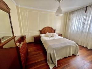 a bedroom with a bed with white sheets and wooden floors at Agradable apartamento céntrico en Cangas in Cangas de Morrazo
