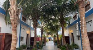 Il Villaggio Luxury Villas في جدة: ممر به أشجار نخيل أمام مبنى