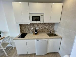 eine weiße Küche mit einer Spüle und einer Mikrowelle in der Unterkunft Amazing sea views from cozy studio. in Puerto de Santiago