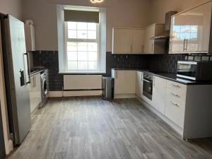 a kitchen with white cabinets and a wooden floor at 3 Bedroom Self Contained Ground Floor Flat With Parking in Plymouth