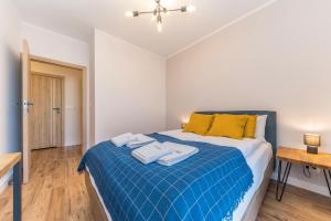 a bedroom with a bed with a blue blanket and yellow pillows at Lumen Billberry Apartments in Gdańsk