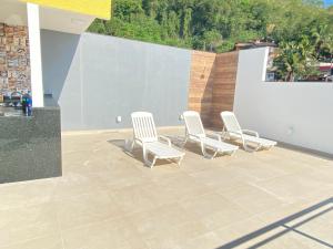 4 chaises blanches assises sur une terrasse avec un mur dans l'établissement Suítes com Vista para o Mar no Marinas - Mirante do Marinas, à Angra dos Reis