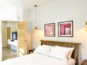 een slaapkamer met een bed met witte lakens en een televisie bij Chez Bure - Bure Homestay in Kanchanaburi