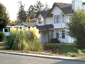 a white house with tall grass in front of a street at Summer Breeze in Sooke