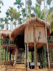 a hut with a straw roof and palm trees at Greenways Tree House and Mud House in Chekadi