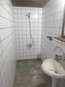 La salle de bains est pourvue de carrelage blanc, d'un lavabo et d'une douche. dans l'établissement Къща за гости Близнаците, à Leshten